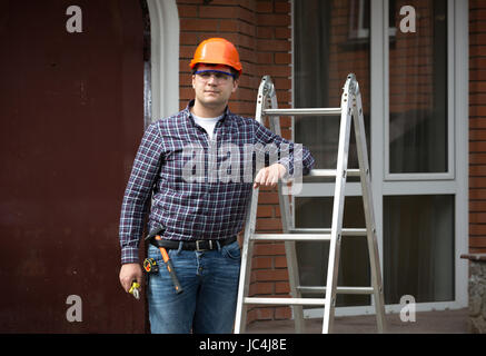 Ritratto di lavoratore sorridente in hard hat appoggiata contro la scala di metallo Foto Stock
