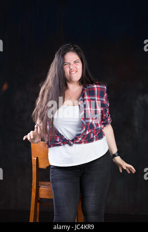 Dimensioni Plus modello femminile che mostra emozioni comune. Impostare in studio su sfondo scuro. Uno stile informale; in jeans, t-shirt e rimosse plaid shirt. Foto Stock