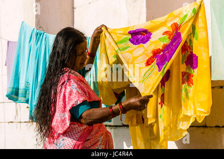 Una donna sta mettendo su servizio lavanderia a secco presso il fiume sacro Gange a ghat sheetla nel sobborgo godowlia Foto Stock