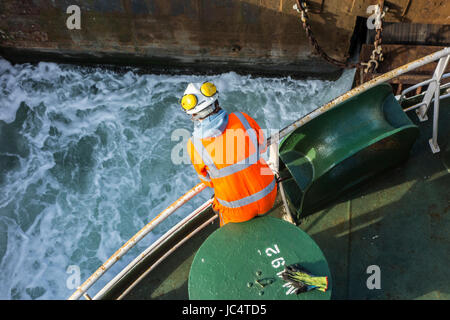 Femmina membro di equipaggio in arancione in generale e di indossare il casco di sicurezza lavorando sul ponte di car carrier / nave da carico nel porto marittimo Foto Stock