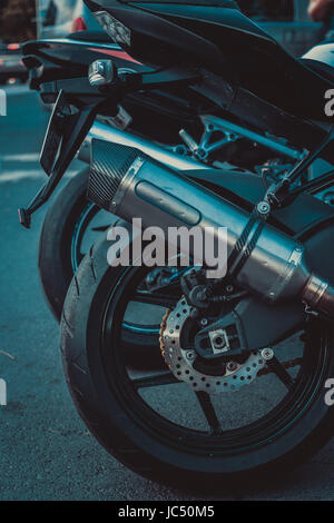 Immagine ravvicinata del motociclo posteriore ruota con pneumatico, Freni a disco e il tubo di scarico. tutti in colore nero. bassa colpo di luce Foto Stock