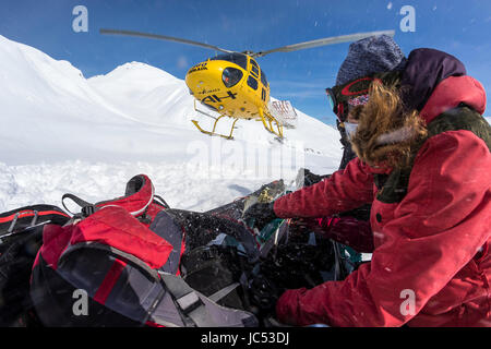 Professional Snowboarder Marie Francia Roy, si accovaccia giù come un elicottero giunge in terra accanto a loro su un soleggiato blue bird giorno in Haines, Alaska. Foto Stock