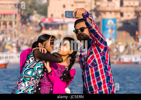 Giovane uomo moderno e le donne stanno prendendo selfies sui banchi di sabbia di fiume santo Ganges, panorama di Dashashwamedh Ghat, principale Ghat, nella distanza Foto Stock
