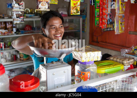 Jula eha servendo un cliente nel suo negozio al di fuori della parte anteriore della sua casa in una tranquilla zona residenziale vicino alla città di Bogor, Indonesia. Il suo negozio aveva mi Foto Stock