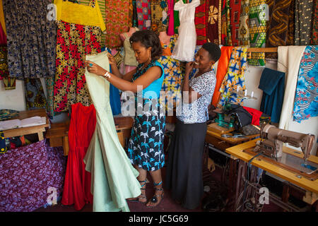 Una piccola azienda sarto femmina che mostra un cliente alcuni tessuto nel suo negozio, Tanzania Africa. Foto Stock