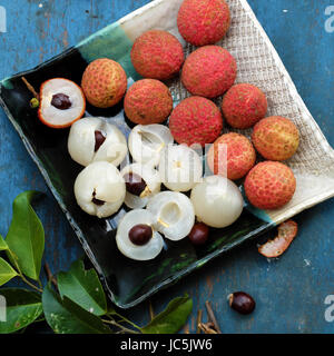 Chiudere la piastra di supporto di frutta su sfondo blu, litchi o lychee frutti o Vai thieu. Rosso scorza di frutta con polpa succosa in bianco che dolce e delizioso Foto Stock