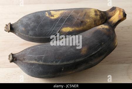 Frutti, due nero marcio Wild Banana, asiatici o Banane Banane coltivata su un tavolo di legno. Foto Stock