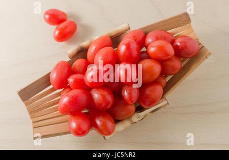 Vegetali freschi maturi uva rossa o Pomodori Pomodori ciliegia su una piccola imbarcazione in legno. Foto Stock