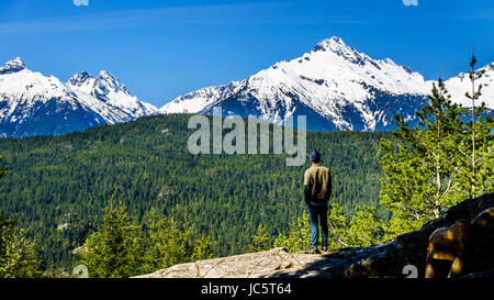 Uomo che guarda il tantalo Mountain Range con cime di montagna alfa, Serratus e Tantalo Monte lungo la Hwy 99 tra Squamish e Whistler Foto Stock