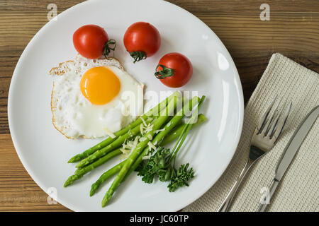Una sana colazione casalinga con uova fritte e asparagi freschi sulla piastra di close-up, servita con i pomodori. Vista superiore Foto Stock