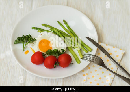 Deliziosa una sana colazione gourmet tradizionale in casa uova fritte e asparagi freschi serviti con pomodori sulla piastra bianca con tovagliolo, forchetta e coltello Foto Stock