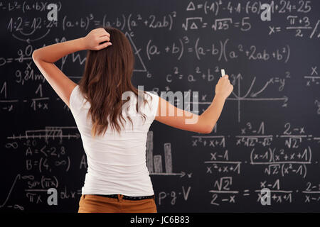 Giovane donna che guarda al problema di matematica sulla lavagna Foto Stock