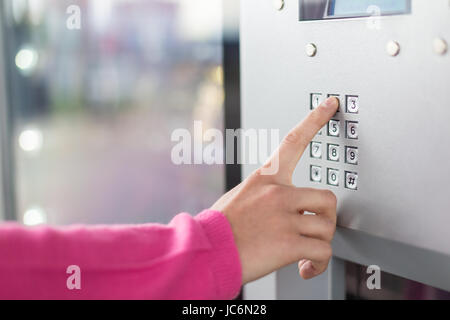 Le donne la mano utilizzando una tastiera numerica su una macchina. Il dito anteriore è posizionata sul tasto del tastierino e sta per premere su di esso. Di piccole dimensioni con display a sfondo blu è anche visibile. Foto Stock