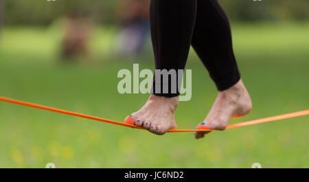 Signora pratica di gioco in linea il parco della città. Slacklining è una pratica in equilibrio che utilizza tipicamente nylon o poliestere nastro teso tra due punti di ancoraggio. Foto Stock