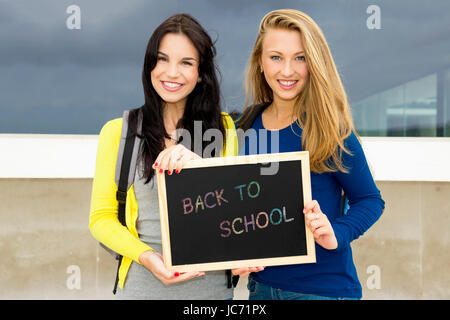 Due belle teenage gli studenti in possesso di una lavagna con lo slogan si torna a scuola Foto Stock