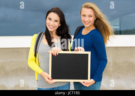 Due belle teenage gli studenti in possesso di una lavagna con lo slogan si torna a scuola Foto Stock