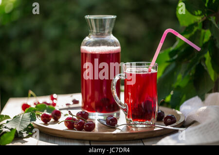 In casa di ciliege acide Frutta sciroppata in coppa di vetro con i jar sul vassoio di bambù e le ciliegie a fianco Foto Stock