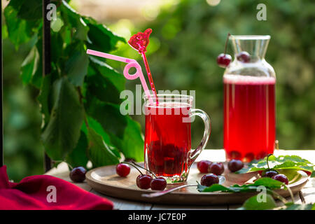 In casa di ciliege acide Frutta sciroppata in coppa di vetro con i jar sul vassoio di bambù e le ciliegie a fianco Foto Stock