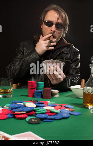 Foto di un uomo giocando a poker indossando occhiali da sole e fumare un sigaro. Foto Stock