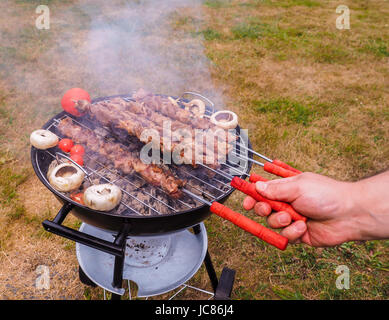 Primo piano di uno chef girando gli spiedini di carne sul barbecue a caldo Foto Stock