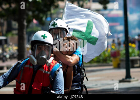 Caracas, Venezuela. 14 giugno 2017. dpatop - volontari provenienti da Università Centrale di Caracas che forniscono il primo aiuto durante le proteste contro il governo, aiuta una donna che soffriva di gas lacrimogeni, a Caracas, Venezuela, 14 giugno 2017. Il gruppo indossa caschi bianco con una croce verde. Foto: Manaure Quintero/dpa/Alamy Live News Foto Stock