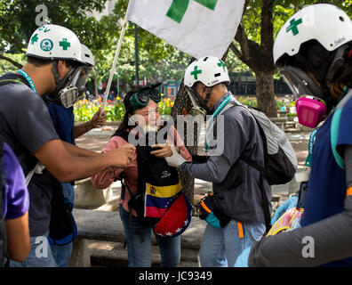 Caracas, Venezuela. 14 Giugno, 2017. Volontari provenienti da Università Centrale di Caracas che forniscono il primo aiuto durante le proteste contro il governo, aiuta una donna che soffriva di gas lacrimogeni, a Caracas, Venezuela, 14 giugno 2017. Il gruppo indossa caschi bianco con una croce verde. Foto: Manaure Quintero/dpa/Alamy Live News Foto Stock