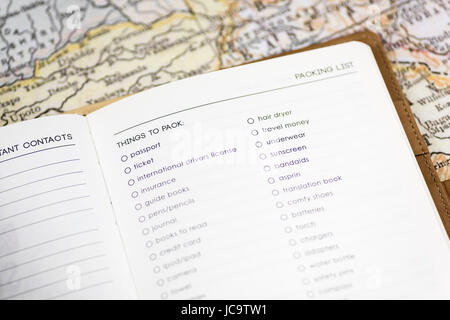 Primo piano di un diario di viaggio su una pagina di una distinta di imballaggio, con sfondo di una mappa d'epoca, incentrato su "cose da mettere in valigia", simboleggiando il concetto di viaggio Foto Stock