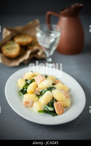 Gnocchi Italiana ammirando servita con salmone e basilico su un piatto di forma ovale con un bicchiere di vino bianco e tostare panini alle erbe Foto Stock