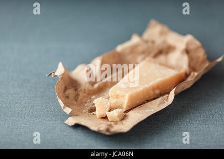 Cuneo di hard italiano Parmigian reggiano su un marrone strappato involucro di carta per uso come un ingrediente di cottura su un tessuto grigio con copyspace Foto Stock