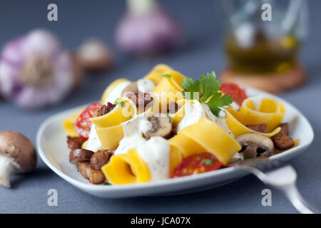 La deliziosa cucina italiana di pappardelle o la pasta cotta con i funghi e i pomodori e spruzzata con una crema conditi con salsa di erbe aromatiche Foto Stock