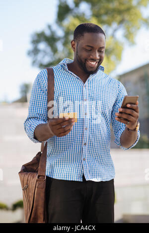 Savvy giovane, utilizzando il suo smartphone per effettuare acquisti on-line Foto Stock