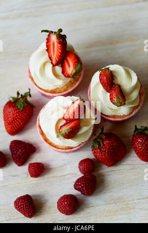 Tortine con panna montata e crema dolce e decorate con le fragole. Su una luce sullo sfondo di legno. Foto Stock