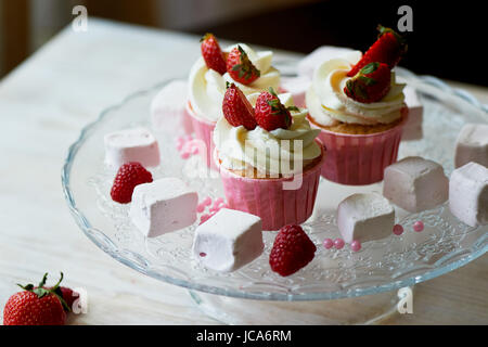 Tortine con panna montata e crema dolce e decorate con le fragole. Su un supporto di vetro e con marshmallow Foto Stock