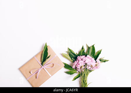 Piccolo bouquet di garofani rosa e un regalo con nastro su sfondo bianco, vista dall'alto Foto Stock