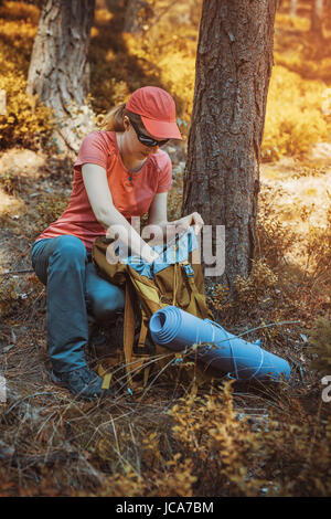 Giovane donna turista nella foresta cercando nello zaino. In autunno i colori del tramonto. Foto Stock