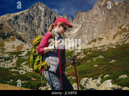 Donna giovani turisti con zaino verde e occhiali da sole passeggiate sulle montagne sullo sfondo Foto Stock