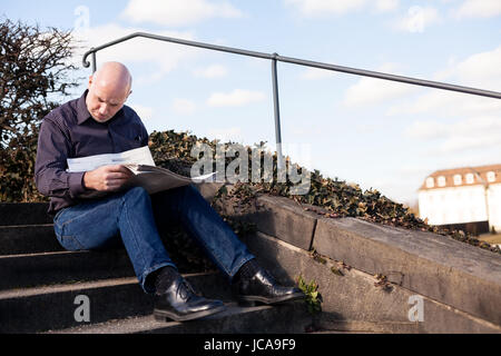 Mann mittleren altera, Senior sitz mit einer Zeitung auf einer Treppe im Frühling im Freien Foto Stock