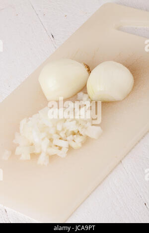 Weiße und rote Zwiebeln geschält und mit Schlale als ganzes und in würfeln Brunoise als Nahaufnahme auf Schneidebrett Foto Stock