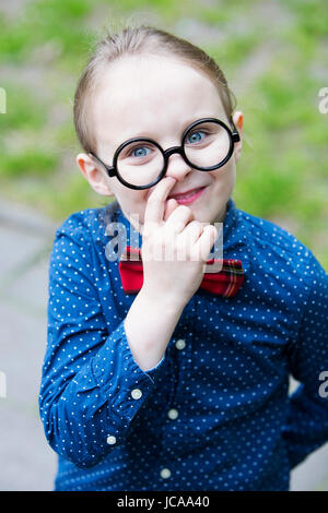 Giovane ragazzo biondo con il filtro bow tie e grandi bicchieri è raccolta il suo naso Foto Stock