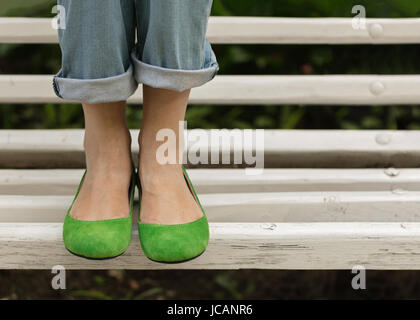 Gambe femmina in blue jeans e scarpe di colore verde su un banco di bianco. Messa a fuoco selettiva. Foto Stock