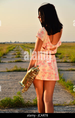 Donna con un sassofono su strada. Vista dal retro Foto Stock