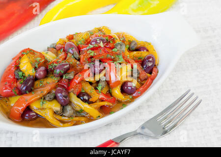 Peperoni cotto in padella con olio, olive e capperi. Cucina tipica italiana, pronto a mangiare. Ciotola bianco su sfondo bianco. Foto Stock