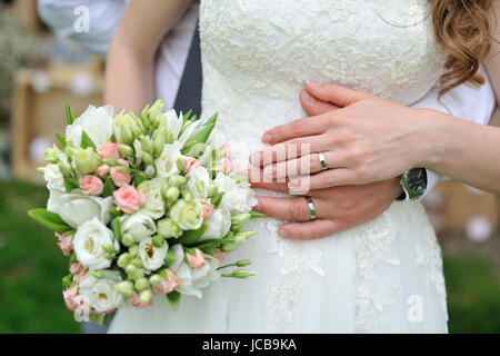 Lo sposo abbraccia la sposa dietro la vita con bouquet di nozze. Foto Stock