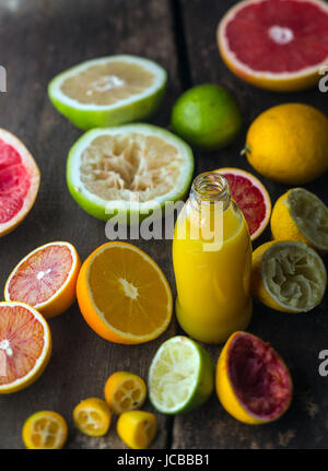 La preparazione di agrumi freschi succhi di frutta in una cucina rustica con una bottiglia di succo di arancia blend circondato da dimezzato le arance, pompelmi, Arancio sanguigno , lime e limone, alcuni dei quali sono stati schiacciati Foto Stock