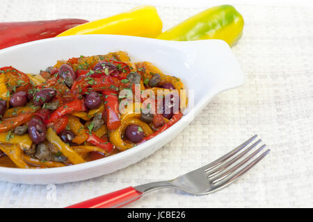 Peperoni cotto in padella con olio, olive e capperi. Cucina tipica italiana, pronto a mangiare. Ciotola bianco su sfondo bianco. Foto Stock