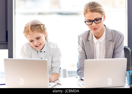 Madre e figlia parlano seduti a tavola con i notebook in ufficio Foto Stock