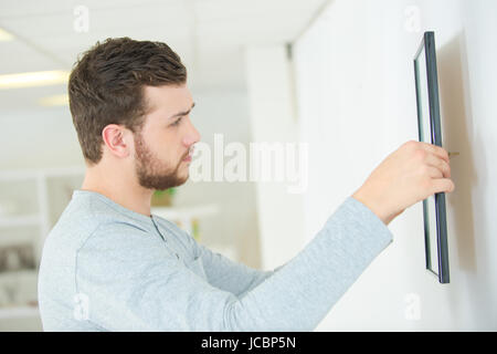 Repairman mettendo cornice immagine sulla parete Foto Stock