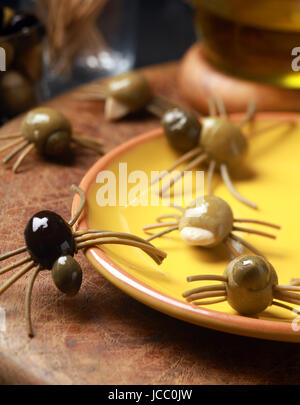 Scary creepy Halloween spider spuntini serviti in un partito di festa fatta dal verde indurito e olive nere con pasta gambe strisciando su tutta la tabella da una piastra di colore giallo Foto Stock