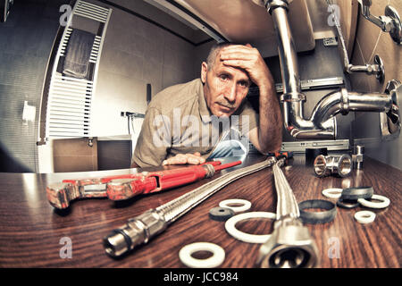 Stanco di una preoccupazione idraulico al lavoro Foto Stock