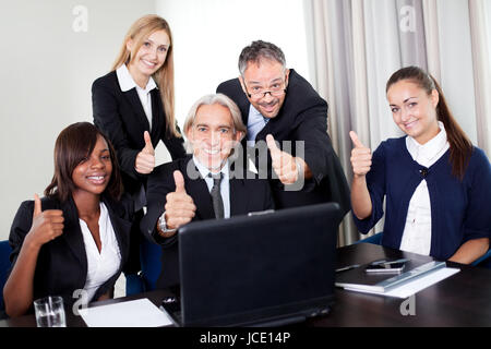 Ritratto di un gruppo di maturi imprenditore in meeing presso l'ufficio con computer portatile - Mostra pollice in alto Foto Stock